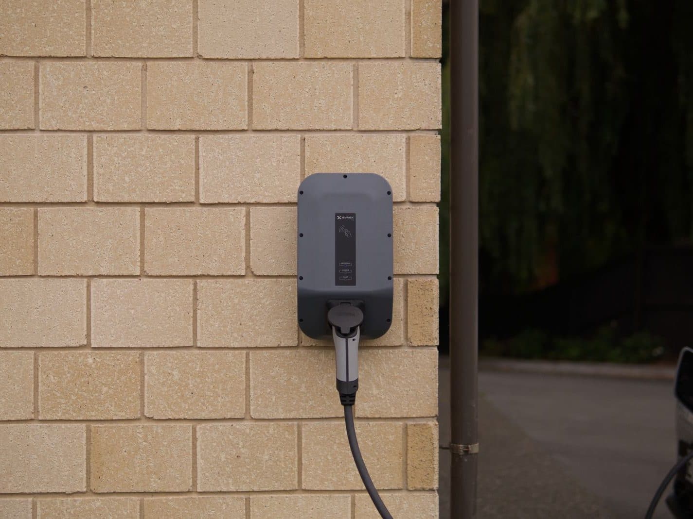 Borne de recharge murale installée à l'extérieur d'un logement, câble branché sur un véhicule électrique