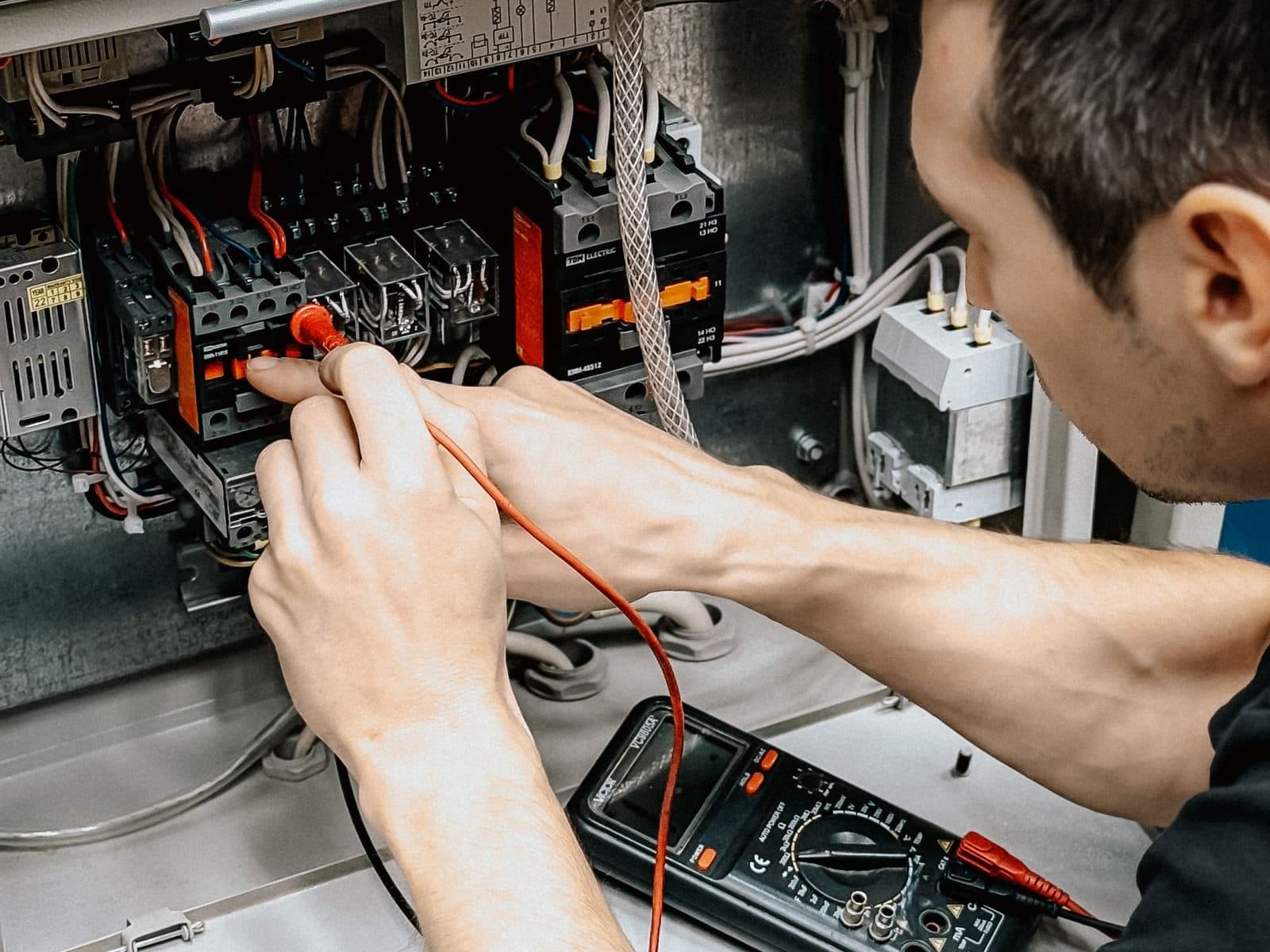 Électricien mesurant au multimètre les circuits d'un tableau électrique ouvert pour localiser l'origine d'une panne
